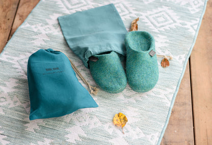 Flat lay of felted wool slippers, linen bag with personalization, patterned rug and autumn leaves