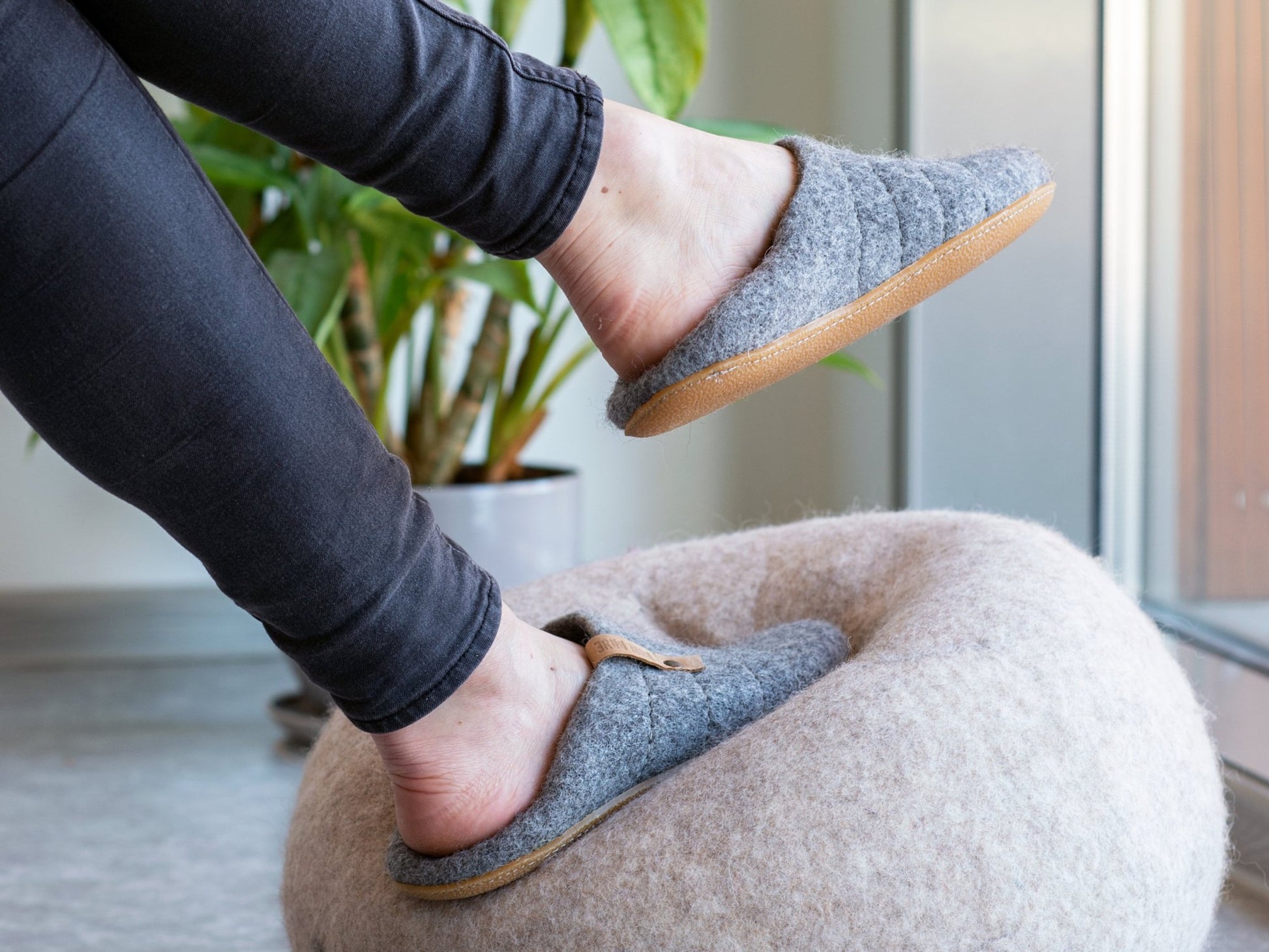 A woman wearing easy to slip on  COCOON slippers, stepping on a felted wool ball